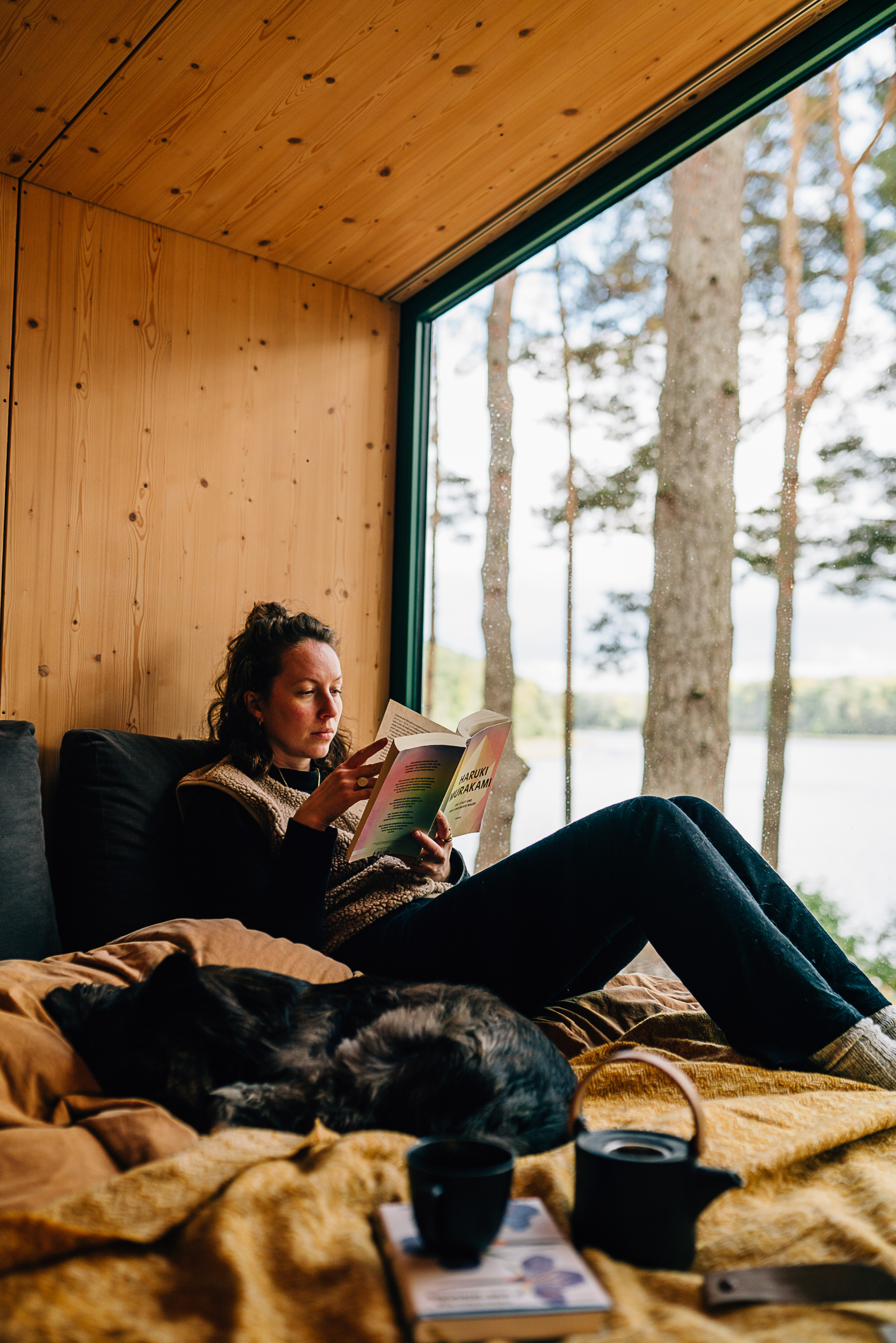 Eine Frau, die auf einem Bett neben einem Hund sitzt und ein Buch von Haruki Murakami liest.