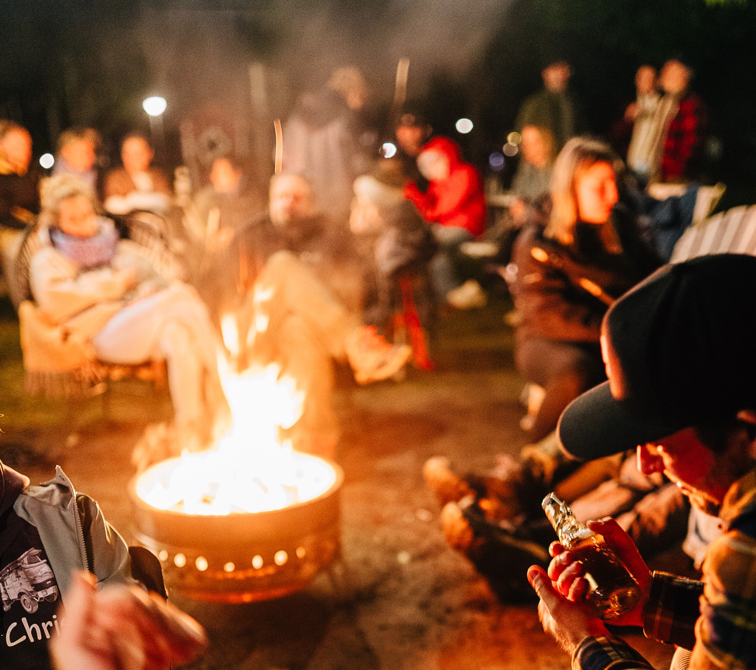 Im Ahoi Camp Canow sitzen die Menschen nachts im Freien im Kreis um eine Feuerstelle herum; einige unterhalten sich, andere entspannen sich. Das warme Schein der Flammen unterstreicht die Kameradschaft und sorgt für einen perfekten Abend, nachdem Sie sich die Preise für Ihren Aufenthalt angesehen haben.
